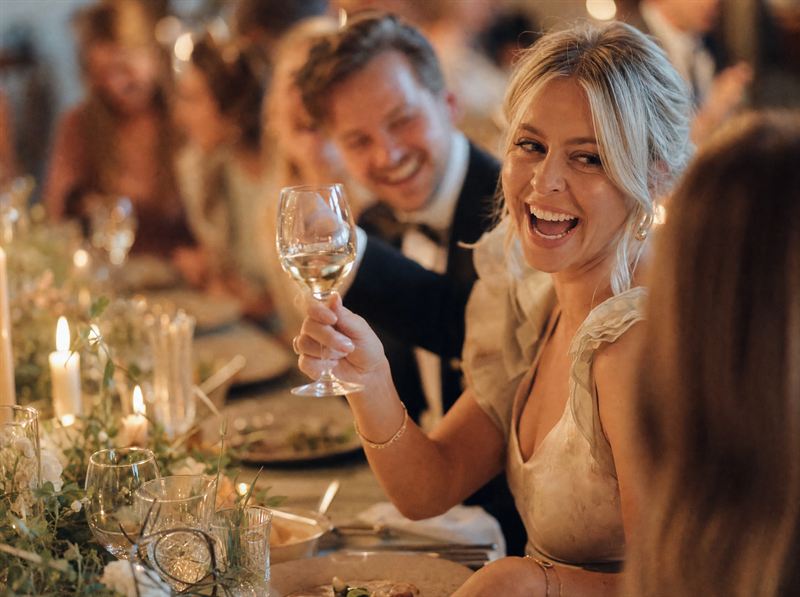 Skrattande gäster höjer glasen vid ett festdukat bord i levande ljus – inspirationsbild