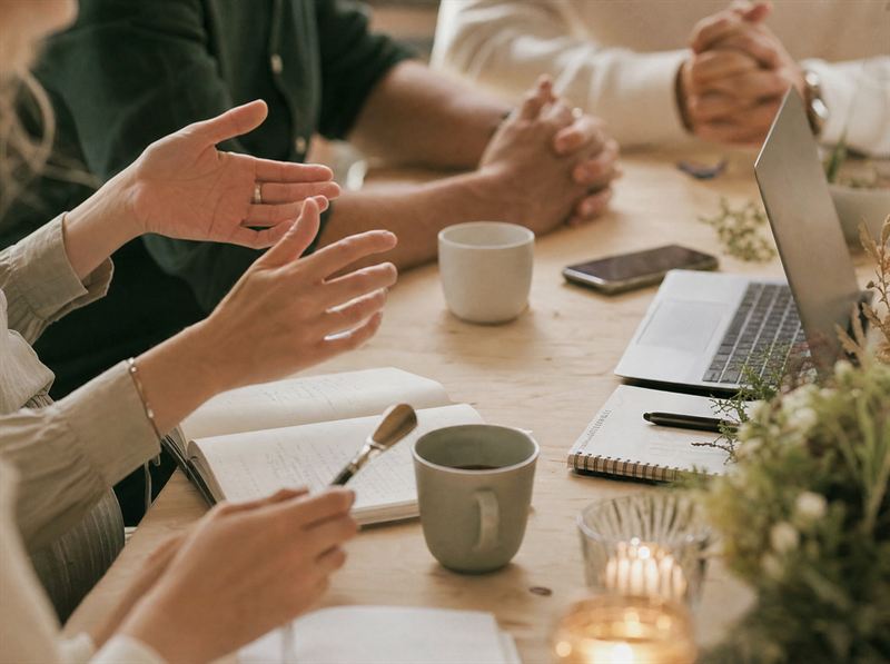 Möte i avslappnad ton med anteckningsböcker, kaffekoppar och laptop vid ett träbord – inspirationsbild
